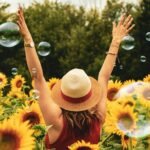A joyful woman in a sunflower field with bubbles, expressing happiness on a summer day.